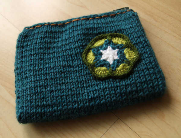 Front of the knitted pouch with a crochet flower attached