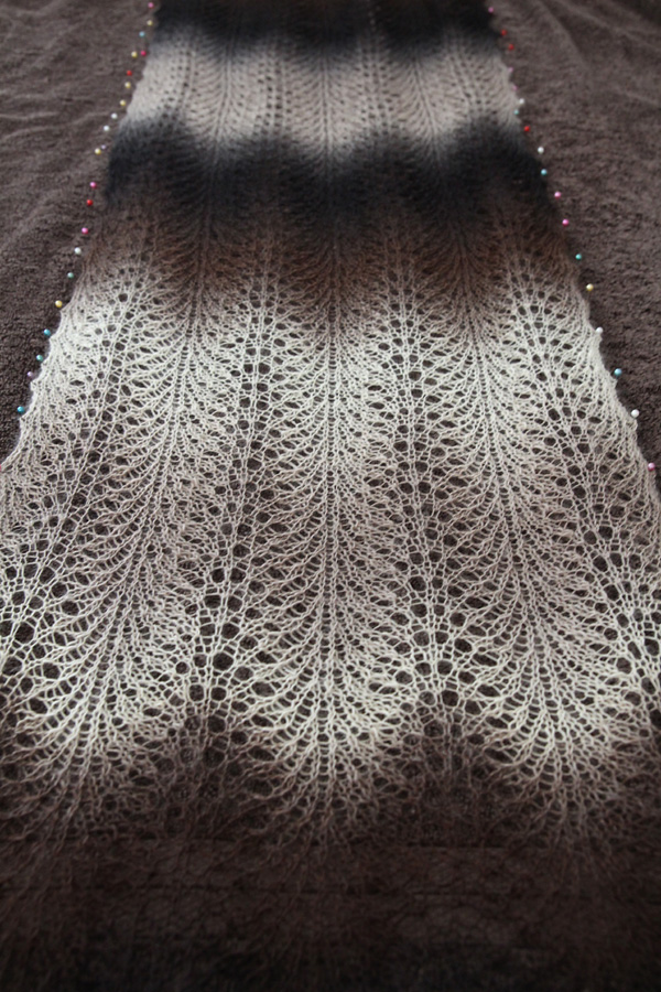 A lace scarf pinned to a towel for blocking.